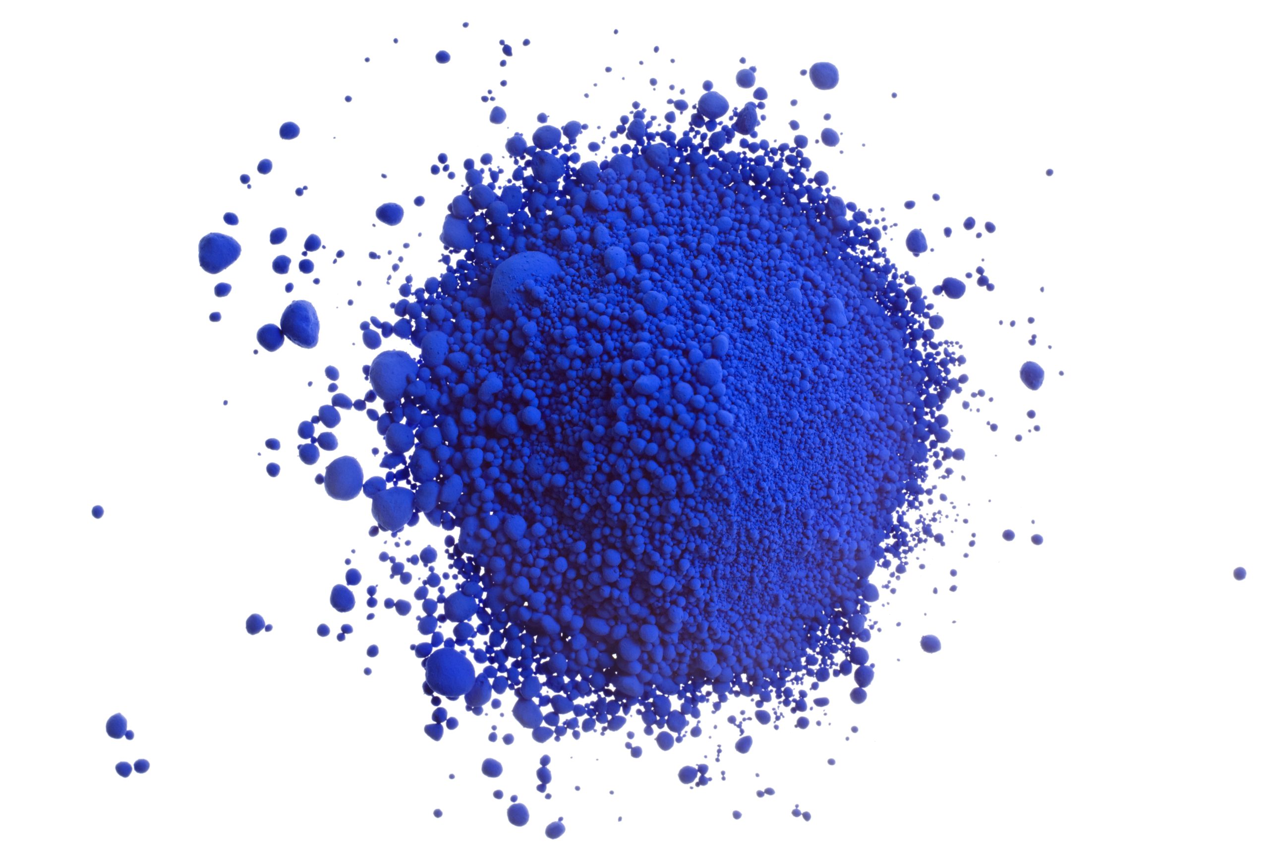 Powder blue pigment: a dense cloud of blue powder exploding outward on a white background, with scattered beads around the edges.